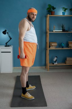 Şortlu ve tişörtlü komik adam evde salonda kilo vermek için dambıl egzersizi yapıyor. Yan görünüm, boşluk kopyala