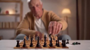 Yaşlı bir adam, kapalı bir alanda sıcak bir ortamda satranç oynarken yoğun bir şekilde odaklanır.