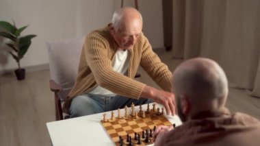 Yaşlı bir adamla genç bir adam evde masada oturmuş satranç oynuyor. destek ve hobi. Boşluğu kopyala