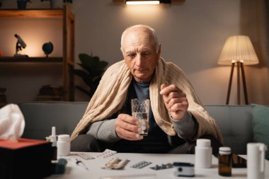 Yaşlı bir adam bir kanepeye oturur, battaniyeye sarılmış, elinde bir hap ve bir bardak su ile. İlacını almaya hazırlanırken çeşitli ilaçlar önlerindeki masaya yayılıyor..