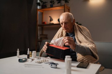 Yaşlı bir adam bir kanepeye oturur, bir battaniyeye sarınır, kutudan bir mendil kullanır. Önündeki masaya çeşitli ilaçlar yayılmış. Hastalığını evde tek başına idare ettiğini gösteriyor..