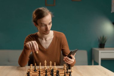 Hippi adam akşamları oturma odasında otururken telefonunu kullanarak online satranç oynamayı öğreniyor. Evde en sevdiğim hobi. Boşluğu kopyala