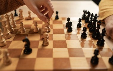 İki oyuncunun stratejik bir hamle yaptığı bir satranç maçına yakından bakmak. Oyunculardan biri beyaz atlı bir atı hareket ettirirken diğeri oyuna odaklanıyor.