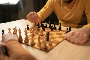 Evde satranç oynayan iki adamın yakın çekim görüntüsü. Kapalı alanda stratejik hamleler yaparlarken dikkatler onların ellerine ve tahta satranç tahtasına çevrildi. Hobi ve eğlence konsepti