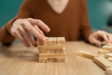 Bir gencin elini dikkatlice yakın plan çekerek tahta blok istifleme oyunundan bir blok kaldırıyor. Rastgele bir oyun sırasında konsantrasyon ve eğlence kavramı.