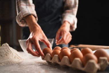 Pişirmeye hazırlanan bir insanın elleri, masaya un konmuş bir kutudan yumurta alıyor. Pişirme süreci kavramı.