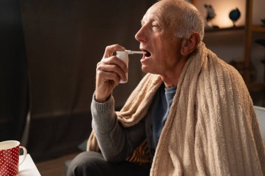 Boğaz spreyi. Yaşlı hasta bir adam soğuktan kurtulmak için boğazına sprey sıkar. Boşluğu kopyala