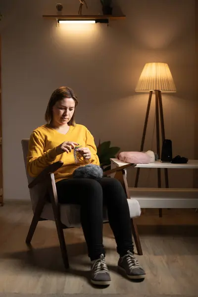 stock image Hobbies and leisure concept. Girl crocheting with thin yarn sitting on armchair in cozy living room in evening. Copy space