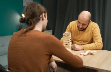İki arkadaş ahşap bir masada oturmuş, tahta blok oyunu oynuyorlar. Oyuna çok bağlılar. Kuleyi çökmekten korumak için tahta blokları dikkatlice kaldırıyorlar ve dengeliyorlar..