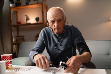 Üst düzey adam evdeki kan basıncını ölçüyor. Yaşlı erkek tansiyonunu yüksek tutuyor. Tonometre kullanıyor.