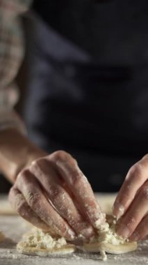 Hamur köftesi yapmak için süzme peynirle doldurulmuş hamur dairelerini mühürleyen kadın ellerine yakın plan. Koyu renk önlük ve ekose gömlek giyiyor. Ev yemeği ve pasta hazırlama kavramı.