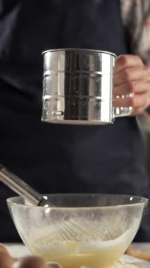 Dişi ellerin temiz bir kâseye un karıştırıp sonra da malzemeleri çırpması. Koyu renk önlük ve ekose gömlek giyiyor. Ev yapımı ve pasta hazırlama kavramı.