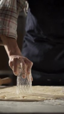 Yuvarlak hamurun dairelerini kesmek için cam kullanan kadın elleri. Koyu renk önlük ve ekose gömlek giyiyor. Ev yapımı ve pasta hazırlama kavramı.