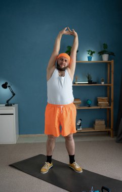 Millennial 'daki parlak spor kıyafetli adam evdeki yoga minderinde esneme egzersizi yapıyor. Rahatlamış bir yaşam tarzı ve ev zindeliği kavramı.