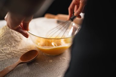 Fırıncı cam bir kasede yumurta çırpıyor, pişirmek için malzemeleri hazırlıyor. Masada bir yığın un ve bir tahta kaşık var. Ev yapımı ve aşçılık hazırlığı kavramı.