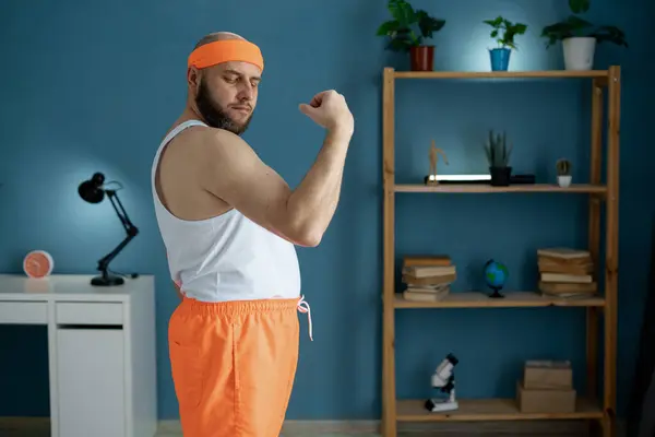 stock image Middle-aged man flexing his biceps during a home workout. He is standing on a yoga mat, showing off his muscle growth. Concept of home fitness, strength training, and healthy lifestyle.