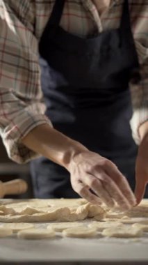 Kalan hamurdan kurabiye şekilleri seçen kadın elleri yakın plan. Koyu renk önlük ve ekose gömlek giyiyor. Ev yapımı ve pasta hazırlama kavramı.