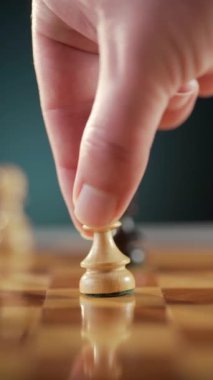Bir el, arkasında siyah bir piyon olan satranç tahtasındaki beyaz piyonu hareket ettiriyor. Stratejik oyun oynuyor.