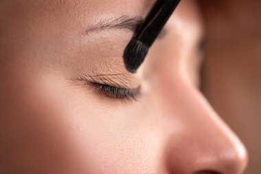 Makyaj ekibi. Makyaj sanatçısı, Göz Gölgesi 'ni kadın gözlerine uyguluyor. Mükemmel makyajlı güzel bir kadın yüzü. Yan görünüm, yakın plan