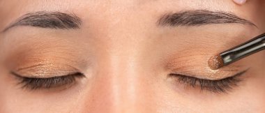 Makyöz, Asyalı kadının gözlerine göz farı sürüyor, yakın plan. Güzellik salonunda profesyonel makyaj konsepti. Yakın çekim.