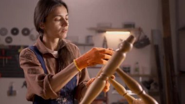 Atmosferik atölyesinde duran beyaz önlüklü kadın zımpara kağıdıyla eski bir sandalyeyi zımparalıyor. Bir parça zımpara kağıdıyla mobilyaları zımparalama işlemi.