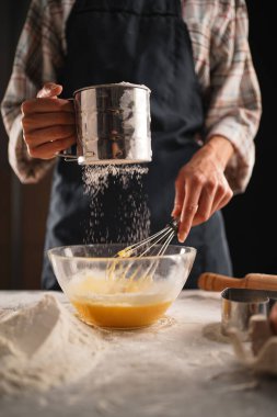 Masada hamur yoğuran tanınmamış bir kadın. Kadın eli, unu şeffaf kâseye yerleştiriyor. Seçici odak.