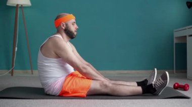 Evde fitness. Odaklanmış milenyum adamı spor minderinde ısınma egzersizi yapıyor, kas bacakları için egzersiz yapıyor. Boşluğu kopyala