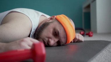 Oturma odasındaki sıkı çalışmadan sonra yorgun, tembel bir adam spor paspasına uzanıp dinleniyor. Boşluğu kopyala