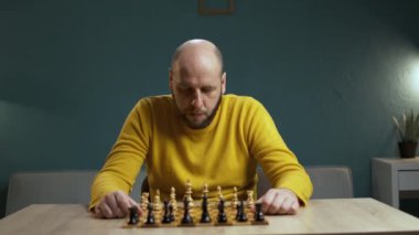 Kel sakallı 40 yaşındaki adam düşünceli bir şekilde satranç oynuyor, beyin fırtınası yapıyor, strateji oyunu oynuyor. Hobi ve eğlence konsepti