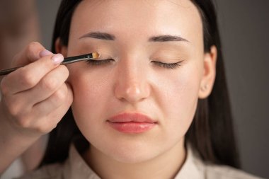 Makyöz, Asyalı kadın için göz farı sürüyor. Mükemmel bir akşam makyajı. Mükemmel ciltli güzel bir kız. Yüzü yakın çekim