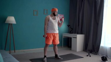 Orta yaşlı bir adam evde dambıl egzersizi yapıyor, pazılarını eğitiyor. Atletik kel adam oturma odasının iç kısmında dambılları kaldırıyor. Boşluğu kopyala