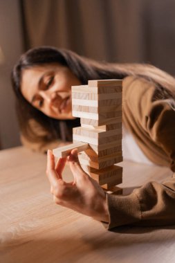 Ahşap blok oyunu oynayan bir kadın, tebessümle dikkatle kuleden parçayı kaldırıyor. Keyif ve eğlence aktivitelerinde yer alma vurgusu.