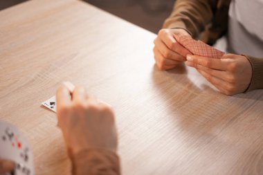 İki arkadaş iskambil oynuyor, yukarıdan bakıyorlar. Elleriniz iskambil kağıdını tutsun, masa yüzeyine odaklanın. Kapalı mekanda rahat bir ortam, boş zamanlardaki aktivitelerin altını çizmek ve sıradan bir kart oyununun keyfi.