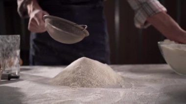 Dişi eller unu elemekle meşguller, masaya daha çok un serpilmiş. Yakın plan.