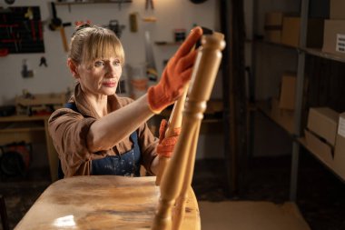 Yaşlı bir kadının atölyesinde eski bir ahşap sandalyeyi ustalıkla restore edişinin yakın çekimi. Sahne, onun titiz işçiliğini ve detaylara olan ilgisini yakalıyor.