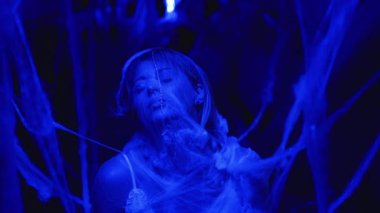 Ürkütücü mavi ışıkla aydınlatılmış örümcek ağlarıyla kaplı bir kadının portresi. Cadılar Bayramı konsepti için uygun ürkütücü ve gizemli atmosfer, kopyalama alanı.