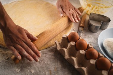 Baker 'ın elleri hamuru ahşap bir oklava kullanarak yuvarlıyor. Sahnede bir kutu yumurta, bir bıçak, kalp şeklinde bir kurabiye bıçağı ve içinde hamur kalıntıları olan bir kase var.