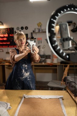 Kadın marangoz blogcu canlı yayın yapan döşeme eğitmeni, atölyede sandalye veya tabure kumaşı için zımba tabancası gösteriyor