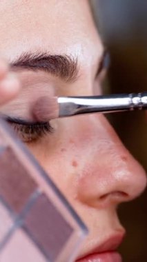 Makyaj sanatçısı, göz farı paletini tutuyor. Kadın Surat, yan görüş. Detaylı mükemmel makyaj. Yakın plan. Dikey video