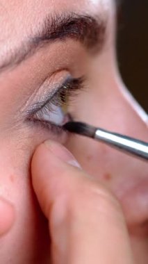 Makyöz alt kirpiklere göz farı sürüyor, göz makyajı, yakın çekim, güzellik konsepti. Dikey video