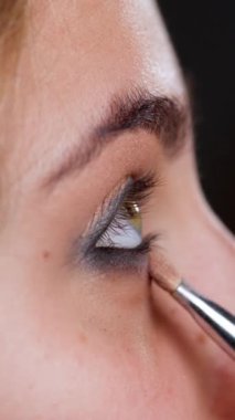 Makyöz göz farı sürüyor. Kozmetik mankeni kızla viyakalı bir tablo. Dikey video