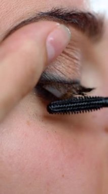 Makyaj sanatçısı, Mascara 'nın kadınlar için uzun kamçılar yapmasını istiyor, yakın plan. Maskara Fırçası. Gözler için makyaj. Dikey video
