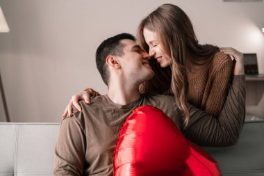 Sevgililer Günün kutlu olsun. Genç bir çift ellerinde kalp şeklinde kırmızı folyo bir balonla evdeki kanepede oturuyorlar. Romantik bir akşam. Boşluğu kopyala
