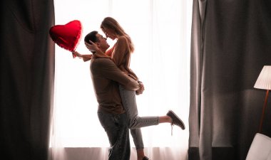 Sevgililer Günü aşkı, pencerede kalp balonu olan bir çift, oturma odasında romantik bir akşam. Boşluğu kopyala