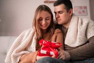 Çekici bir adam hediye kutusunu kız arkadaşına veriyor. 14 Şubat 'ta evdeki oturma odasında kanepede oturan aşık bir çift. Sevgililer günü ve romantik akşam konsepti. Boşluğu kopyala