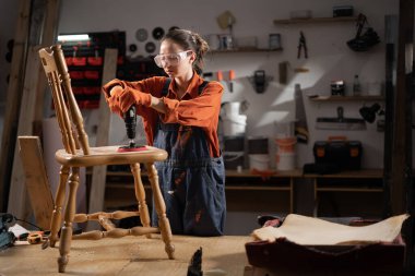 Güvenlik gözlüklü kadın atölyedeki eski mobilyaları restore ediyor zımpara kağıdıyla zımpara ile antika ahşap sandalyeyi yeniliyor ve detaylara ve işçiliğe odaklanıyor.