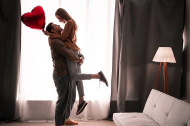 Sevgililer Günü romantizmi, pencerede kalp balonu olan bir çift, oturma odasında aşk kutlaması. Boşluğu kopyala
