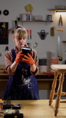 Atölyede çalışan bir kadın elinde eski bir tahta sandalyeyi yenilemeye hazırlanan bir kutu boya tutuyor. Mobilya restorasyonu, antika yenileme, küçük işletmeler, işçilik.