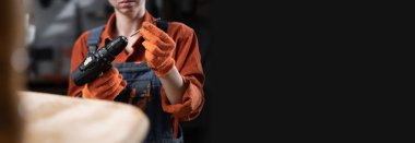 Bir kadın atölyesinde çalışan ahşap sandalyeyi monte etmek üzere matkabı matkaba sokuyor. Pankart