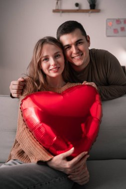 Aşık genç bir çiftin portresi kalp şeklinde bir balon tutuyor ve kameraya bakıyor. Romantik bir akşam ve Sevgililer Günün kutlu olsun. Boşluğu kopyala